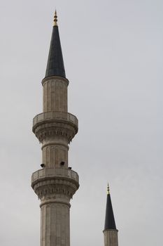 Vertical shot of ornate minaret towers reaching up into a cloudy sky, showcasing Islamic architecture.