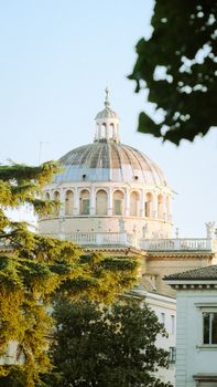 Low angle view of the historic Parma Cathedral dome surrounded by lush trees under a blue sky.