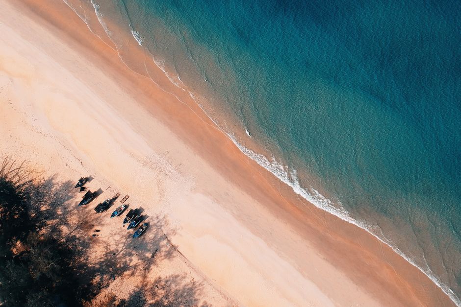 Stunning aerial shot capturing a serene beach, gentle waves, and small boats on the sandy shore.