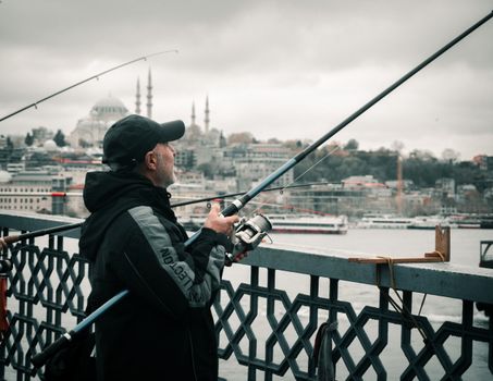 Man fishing on Galata Bridge, İstanbul with city skyline backdrop.