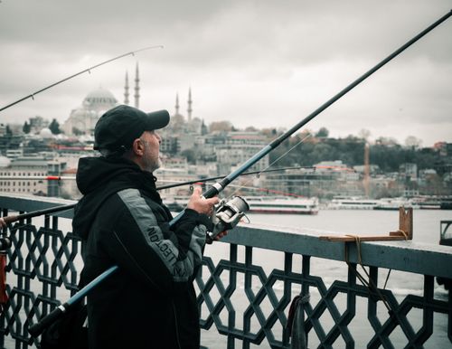 Free Man fishing on Galata Bridge, İstanbul with city skyline backdrop. Stock Photo