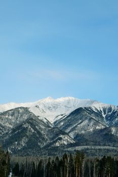 Admire this winter landscape with snowcapped mountains under a clear blue sky, perfect for nature enthusiasts.