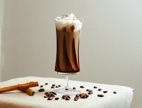 Delicious iced coffee with cream in glass with coffee beans and cinnamon.