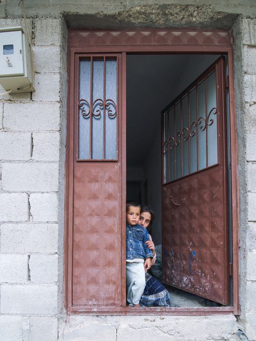 Free A young child peeking from behind a partially open corrugated metal door with protective grills. Stock Photo