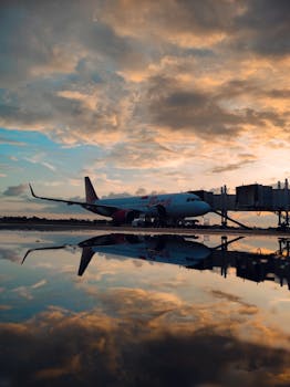 Commercial airplane parked at Surakarta airport with sunset reflection in puddle.