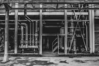 这是一张黑白照片，画面中是一座废弃的工业建筑，管道和钢结构都裸露在外