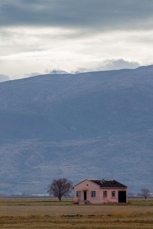 Free Lonely house in a scenic field with mountain backdrop on a cloudy day. Stock Photo