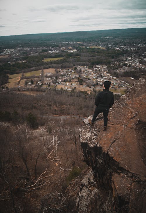 Drone Shot of a Man Standing on a Cliff overlooking a Town and Forests 