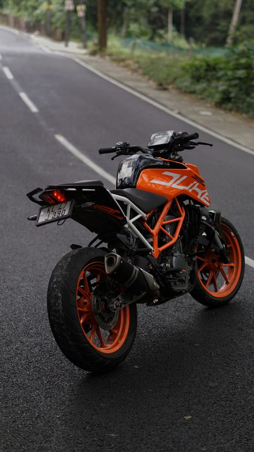 Free A sleek orange motorcycle parked on a forested road, showcasing its sporty design. Stock Photo