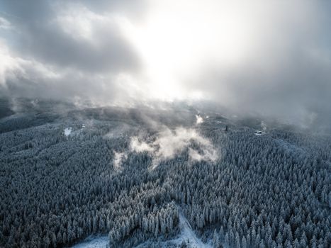 A stunning aerial view of a snow-covered forest in winter, with mist and clouds.