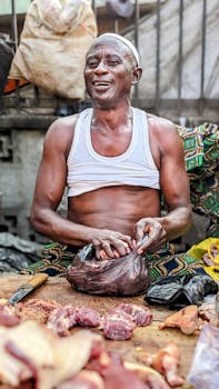 A cheerful butcher in a meat shop, packing raw meat with a smile at a lively indoor market.