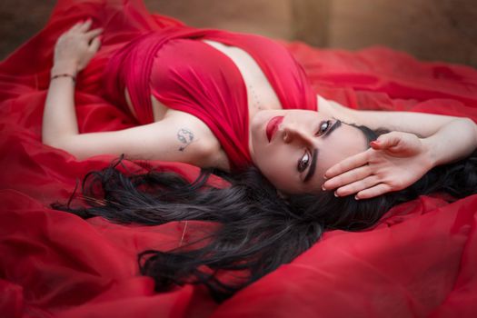 An elegant woman in a red dress lies gracefully outdoors, exuding sensuality and fashion.