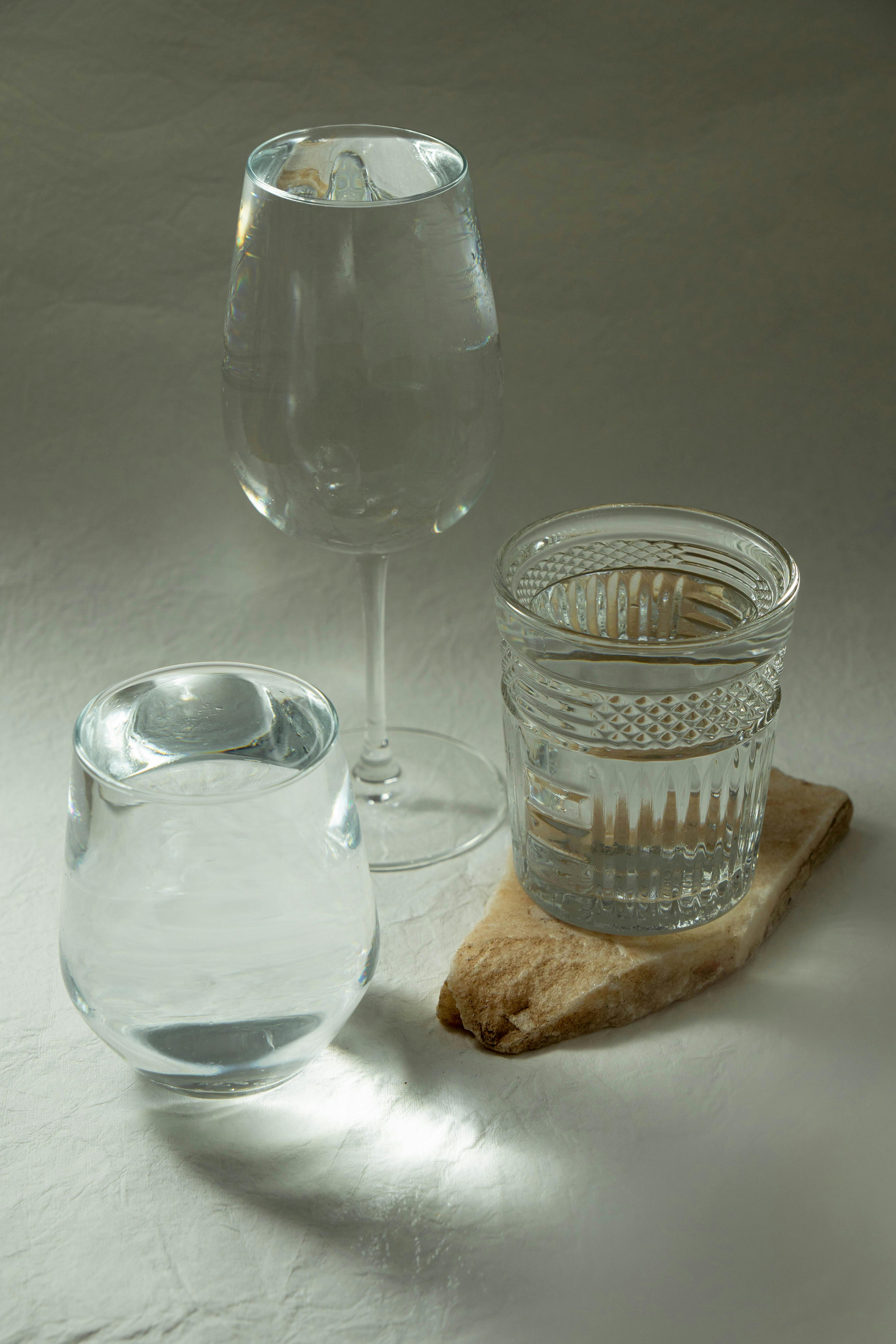 Three elegant glass vessels filled with water, artistically arranged on a textured surface.