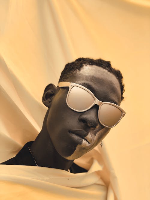 Man with Gold Paint on Face in Sunglasses on Fabric Background