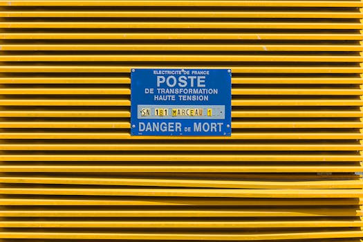 Close-up of a yellow industrial grate with a blue high voltage warning sign in French.