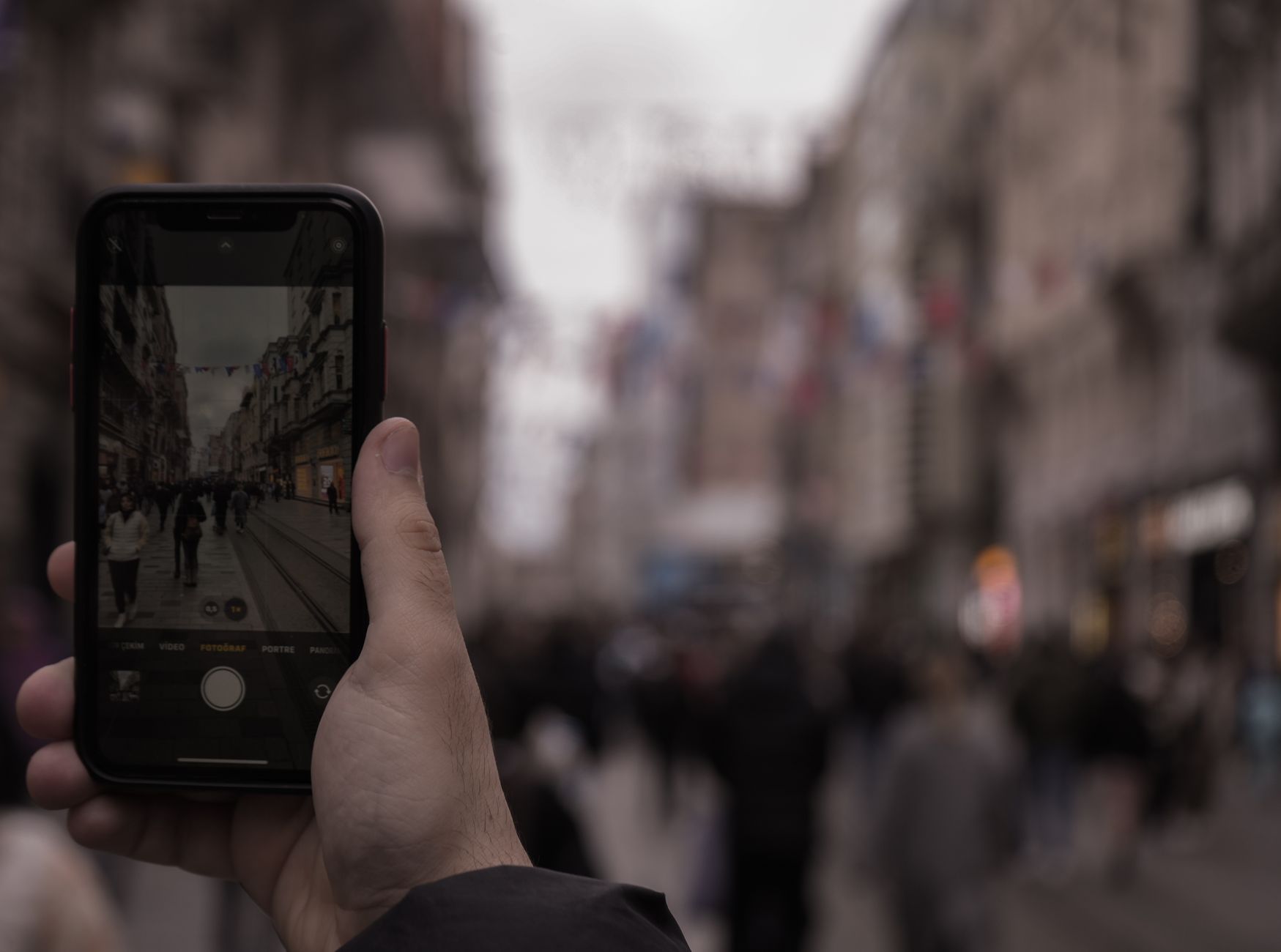 A hand captures a bustling city street scene with a smartphone in a lively urban environment.