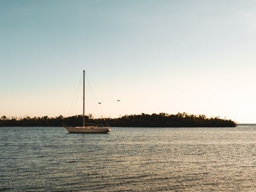 Free A serene image of a sailboat at sea during sunset, with a clear sky and distant coastline. Stock Photo