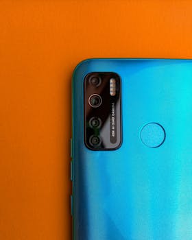 Detailed view of a blue smartphone's camera against an orange background, showcasing modern technology.