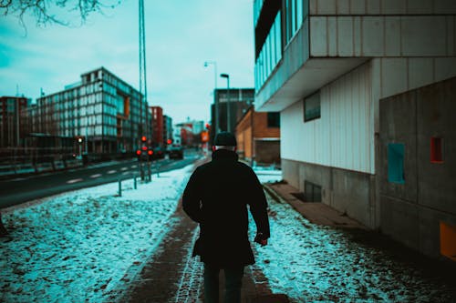 Back View of a Man Walking on Sidewalk During Winter