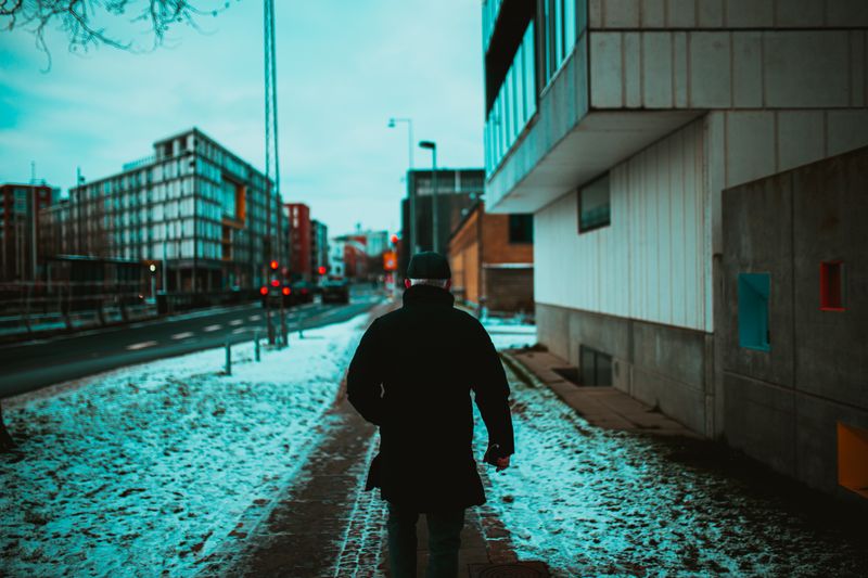 Person walking in winter urban setting with snow on a city sidewalk.