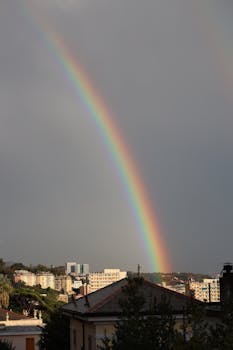 A vibrant rainbow stretches over a city with buildings, creating a striking urban landscape.