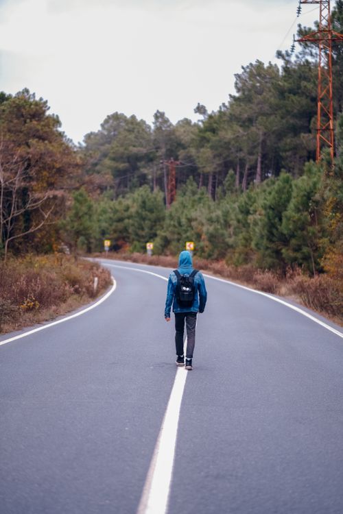 Free Man with a backpack walking alone on a forest road, showcasing solitude and nature. Stock Photo