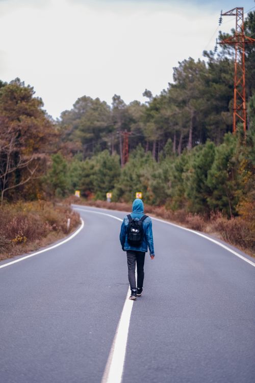 Free Man with backpack walks alone on a winding road through lush forest. Stock Photo