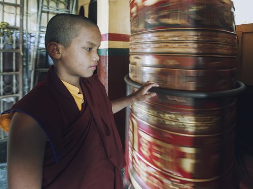 Free A young monk spins a large prayer wheel inside a temple, reflecting spirituality. Stock Photo