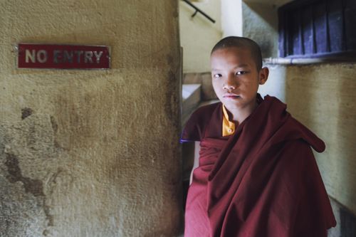 Free A teenager dressed as a monk stands indoors near a no entry sign, conveying serenity. Stock Photo