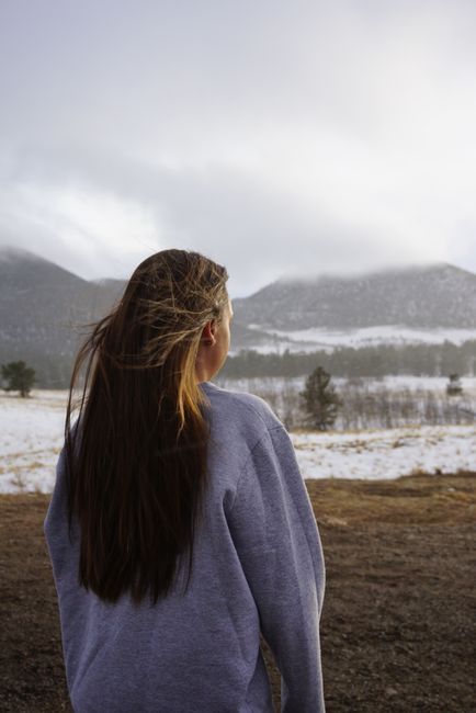 A woman in a sweatshirt gazing at a winter mountain landscape, enveloped in serene beauty.