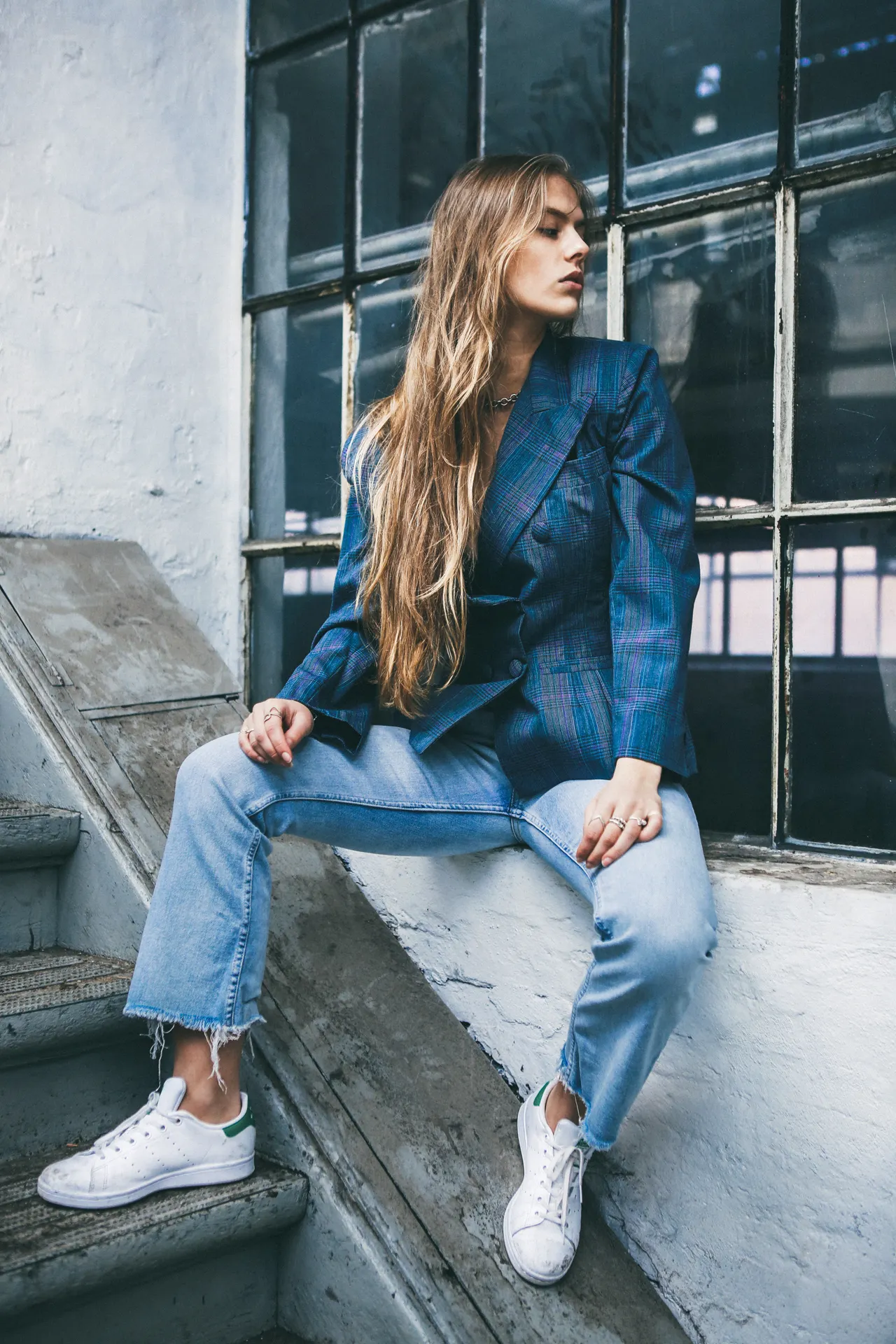 blazer-jeans-sneakers-airport-outfit Woman in a plaid blazer with jeans and white sneakers, a smart casual airport outfit