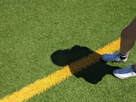 Shadow of sneakers on a green soccer field with a yellow line.