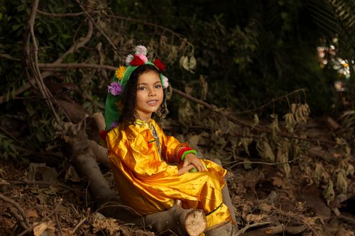 Free A smiling girl sitting in a vibrant costume surrounded by nature, embodying playful joy. Stock Photo