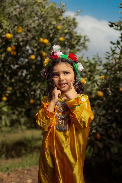 Free A young girl in traditional attire happily posing in an orange orchard. Stock Photo