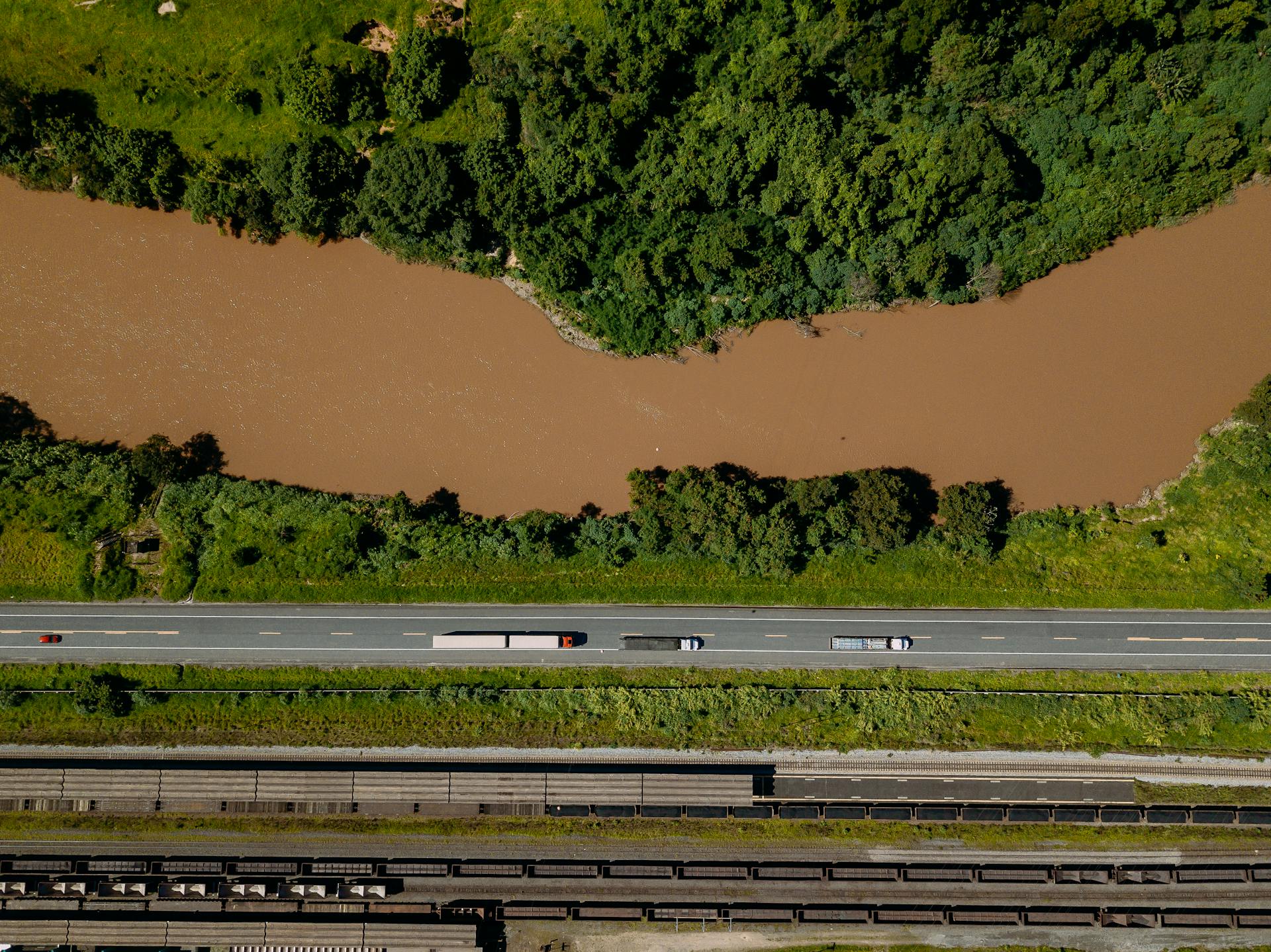Aerial shot of trucks on a road beside a river in Coronel Fabriciano, Brazil.