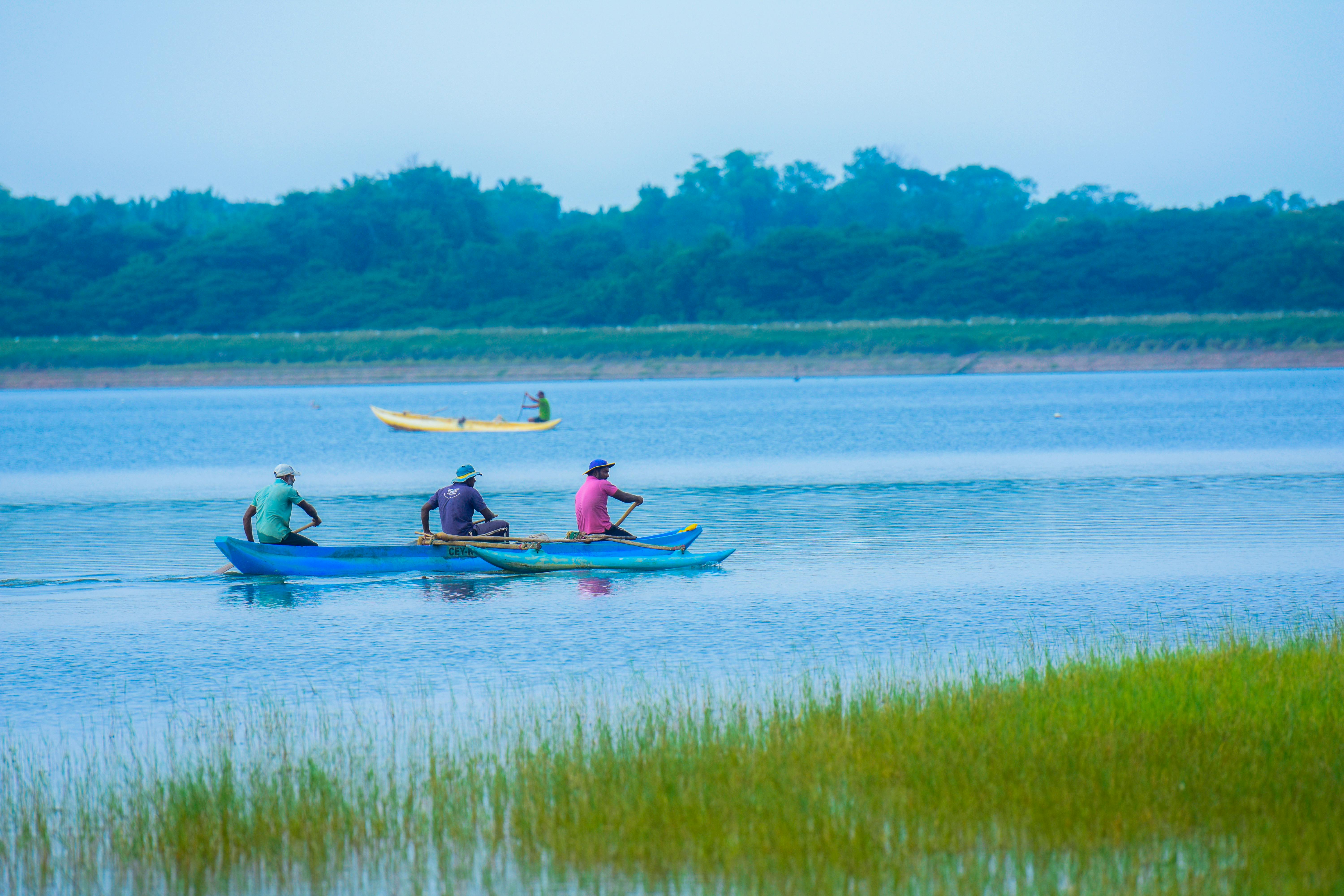 Three men rowing on a serene lake in Hatton, Sri Lanka, surrounded by lush greenery.