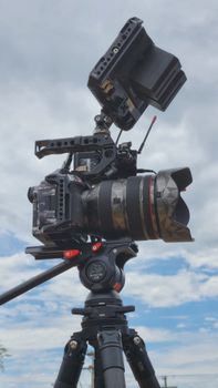 Close-up of a video camera on a tripod, set against a cloudy sky, ideal for filmmaking.