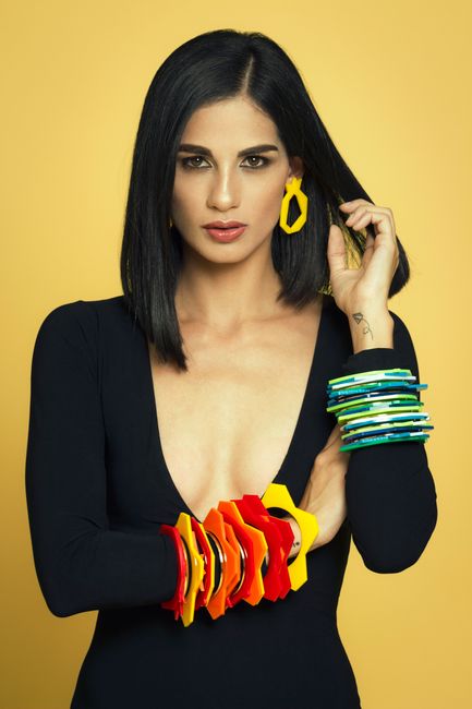 Fashionable woman posing with colorful bracelets and earrings against a yellow background.