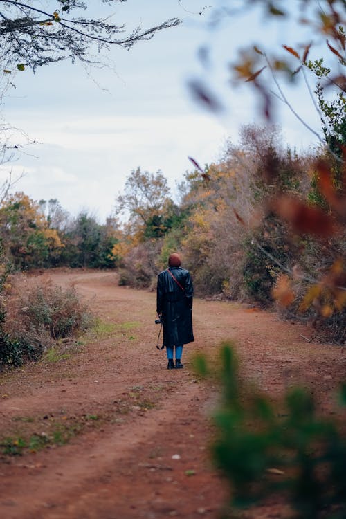 Person in Black Trench Coat Walking on Dirt Path