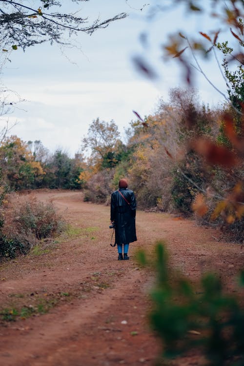 Person in Black Trench Coat Walking on Dirt Path