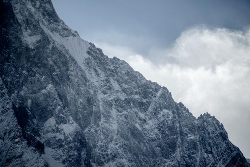 Free Dramatic view of a snow-covered rocky mountain peak under a cloudy blue sky. Stock Photo