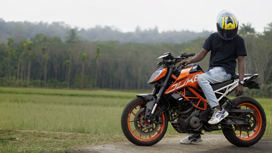 Man on an orange motorcycle resting in a rice field setting with lush greenery.