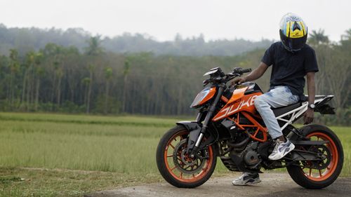 Free Man on an orange motorcycle resting in a rice field setting with lush greenery. Stock Photo