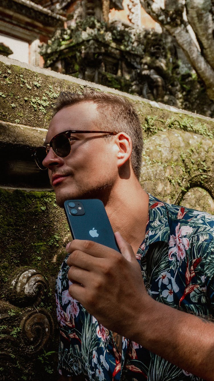 A Man In Aloha Shirt Holding A Black IPhone