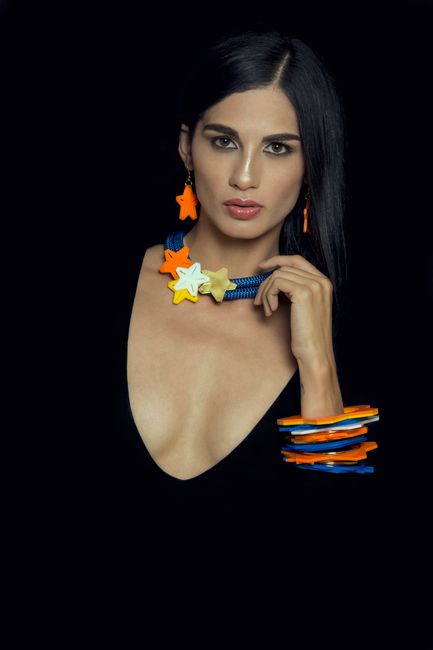 Elegant woman posing with colorful star-themed jewelry on black background.