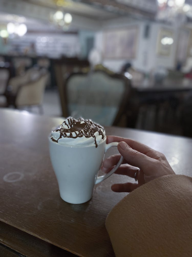 Person Drinking Coffee With Cream In Cafe