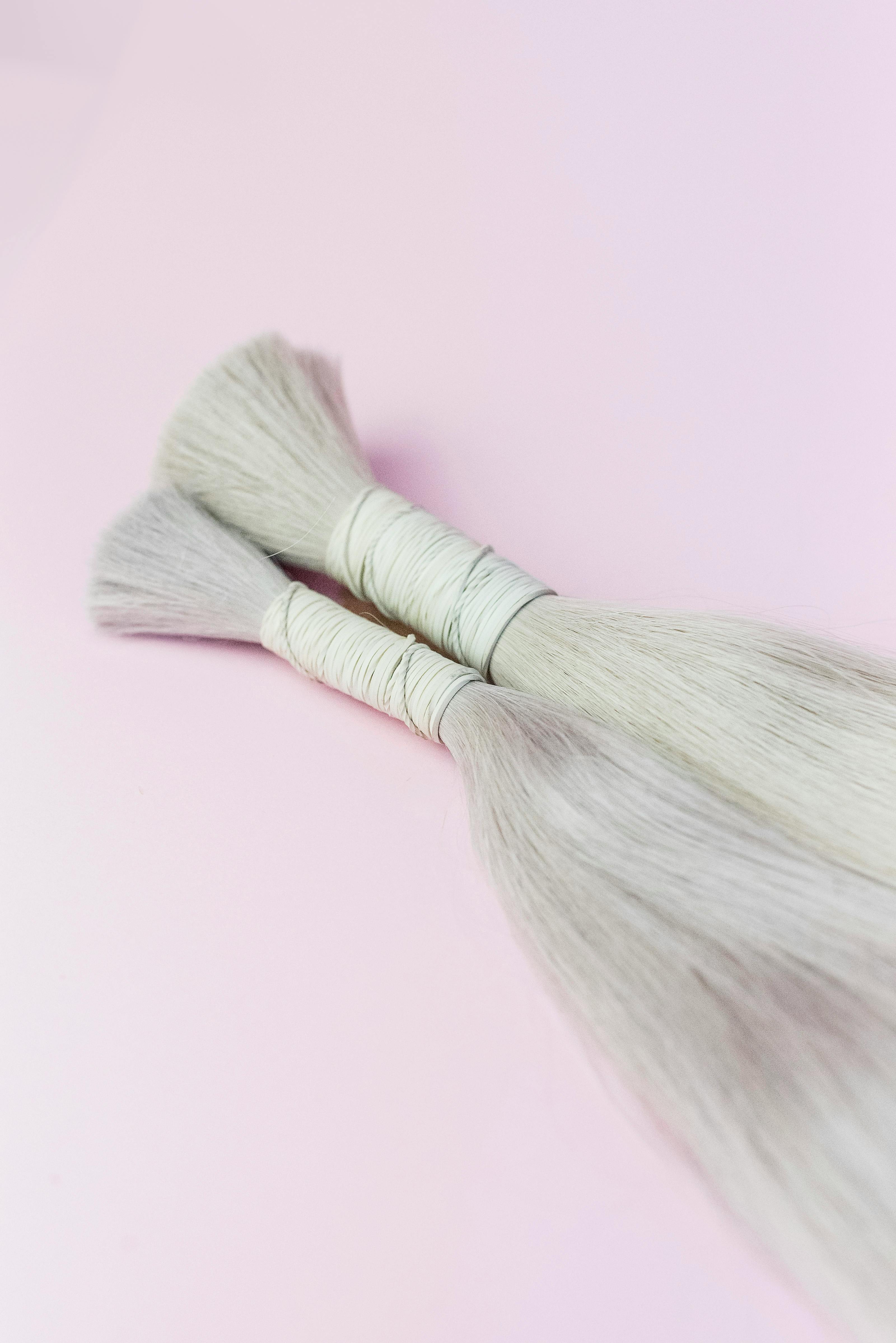 Close-up of two blonde hair extension bundles on a pastel pink surface.