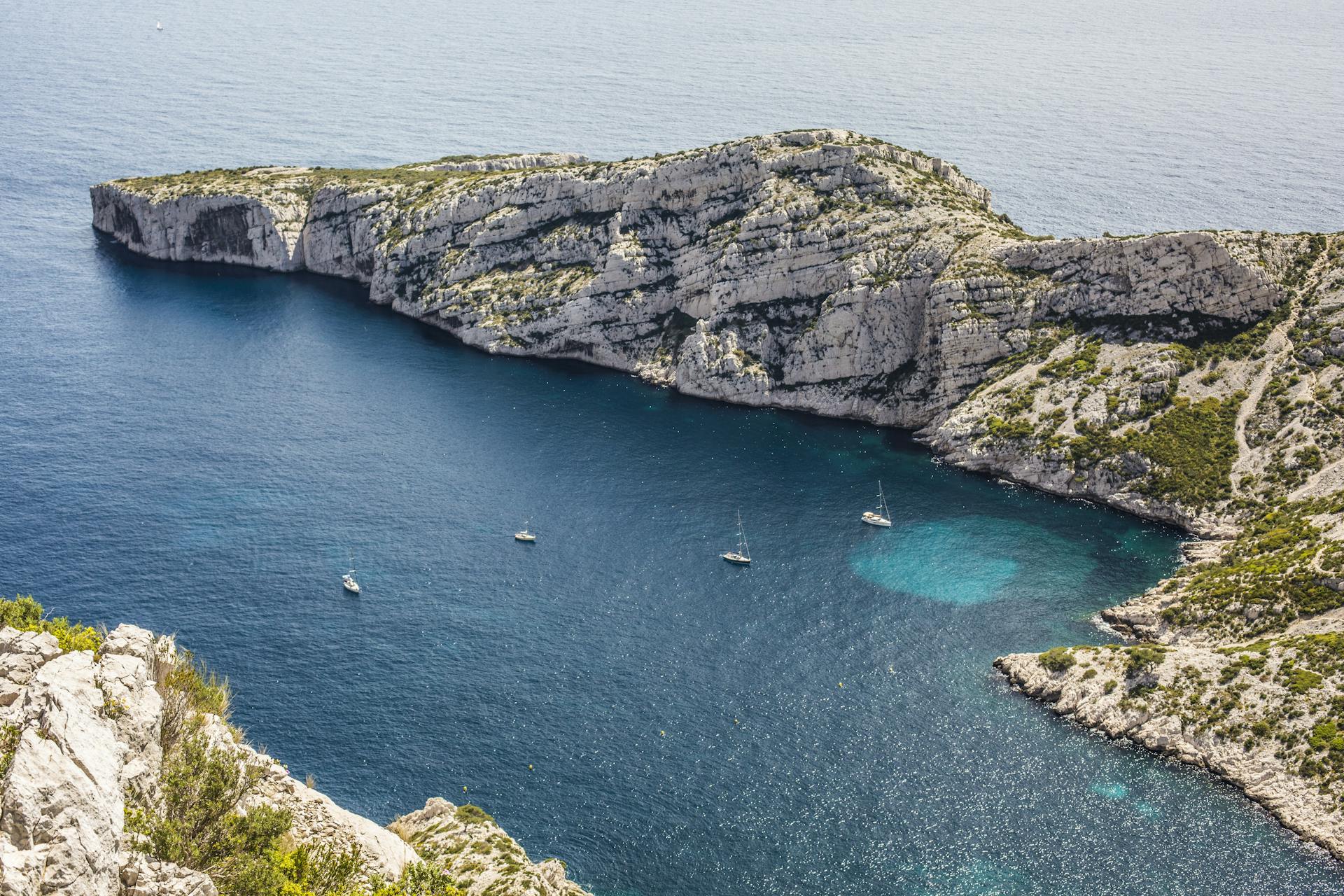 A breathtaking view of sailboats in a deep blue bay surrounded by rugged limestone cliffs.