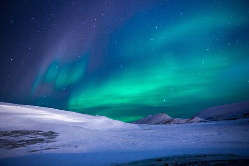 Free A breathtaking view of aurora borealis illuminating a snowy winter landscape under a starry sky. Stock Photo