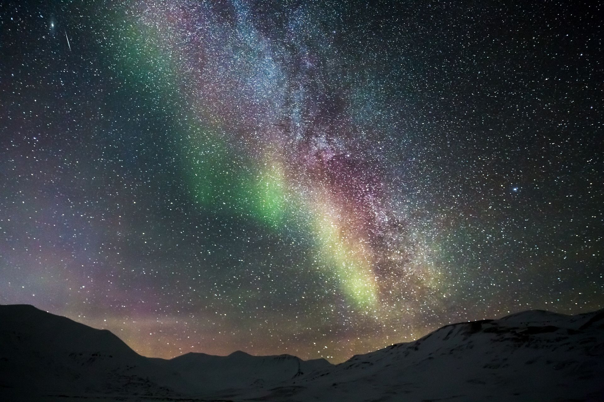 A mesmerizing view of the aurora borealis against a star-filled night sky over mountain silhouettes.
